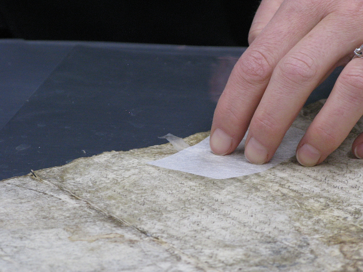 Close up on somebody's hand as they repair a torn parchment.