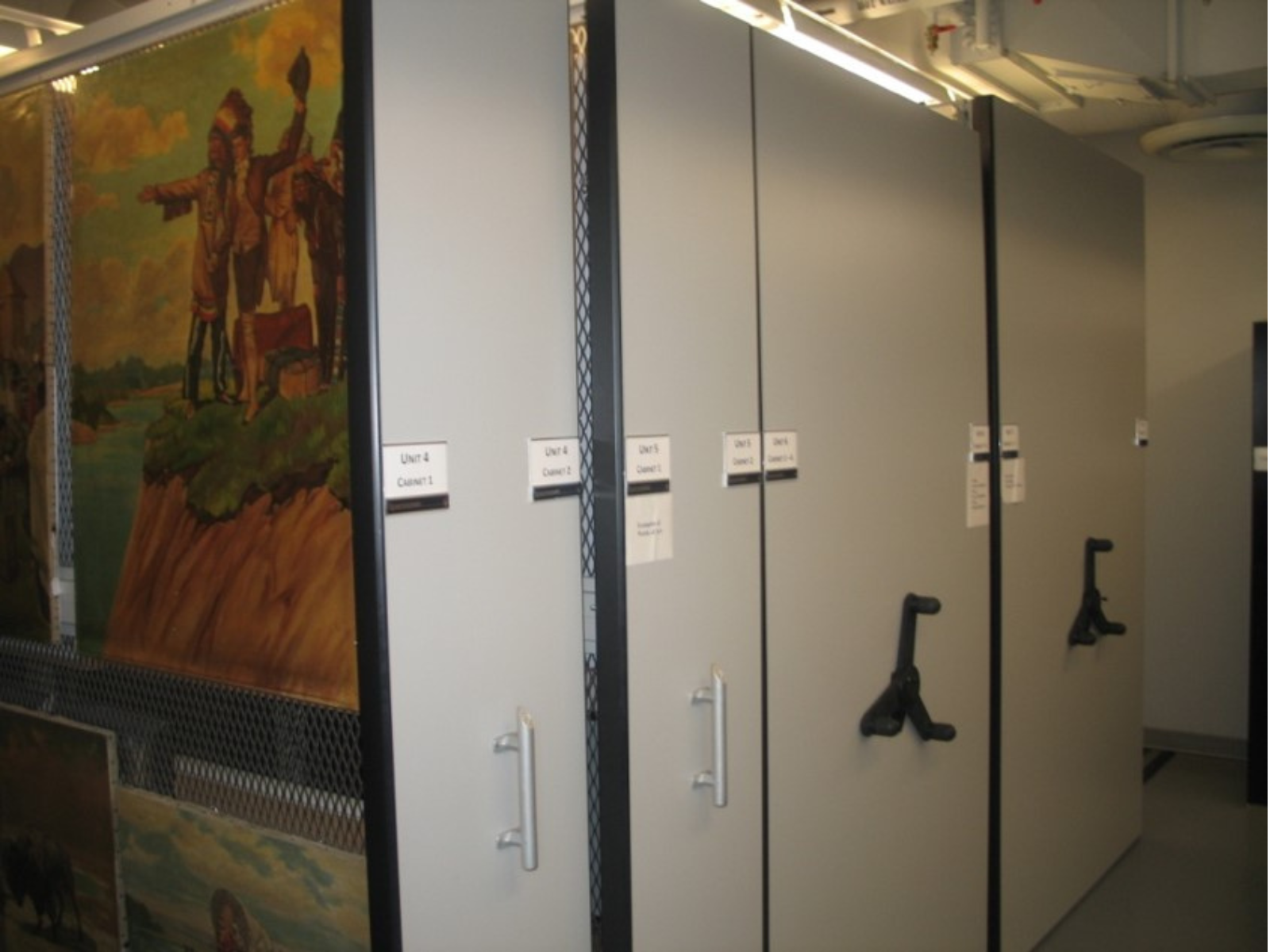 Rolling storage units in collection storage. Inside the nearest unit hang pieces of art.