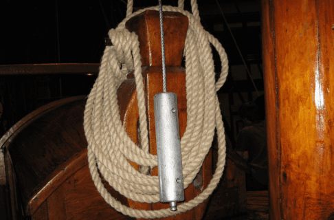 A coil of cream rope on a wooden notch. In the front there's a steel safety line.