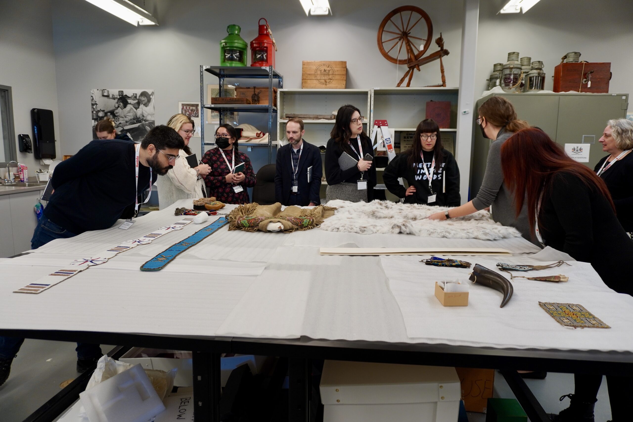 A large table with a group of 9 people looking at artifacts on the table.