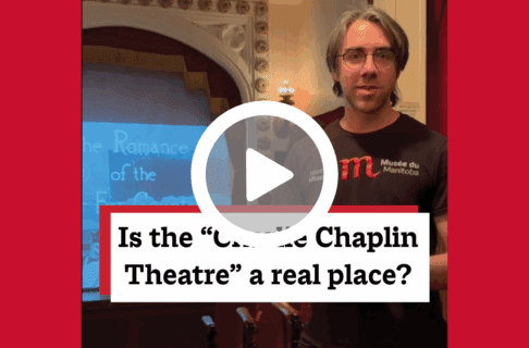 A screenshot of a video, an individual stands in the doorway of the Allen Theatre in the Winnipeg 1920 Cityscape. There's a play button over the screenshot and overlaid text reads, "Is the 'Charlie Chaplin Theatre' a real place?".