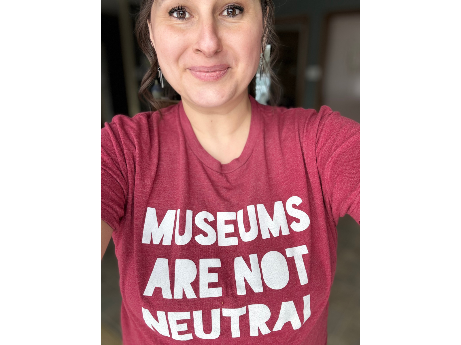 A selfie of Manitoba Museum CEO Dorota Blumczyńska wearing a soft red shirt that reads, "Museums are not neutral" in a large bold font.