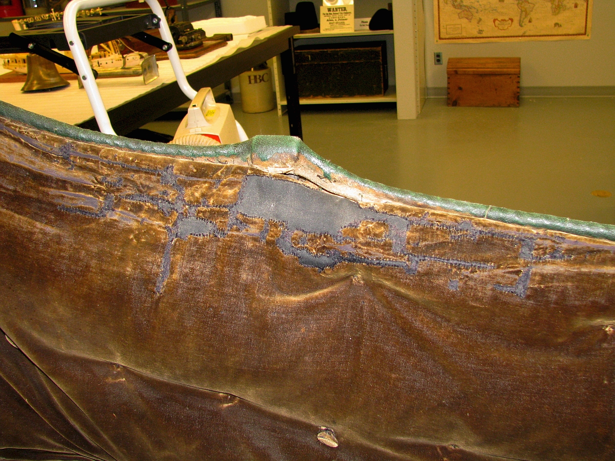 Close up on a side of the inside of a cariole on a display in a museum lab. Some repair work has been done along one of the edges.