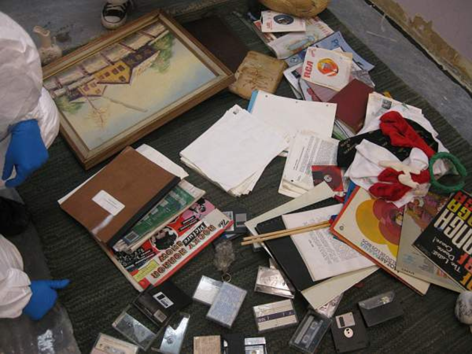 A variety of objects including a rug, painting, notebooks, cassette tapes, floppy dusks, and more piled on the floor.