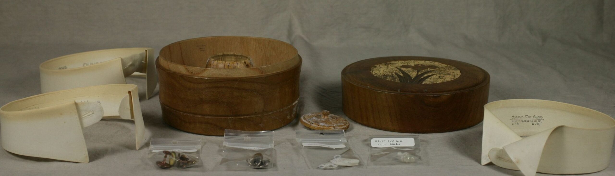 Two wooden collar storage boxes positioned next to three aged-white collars and small baggies with collar studs.