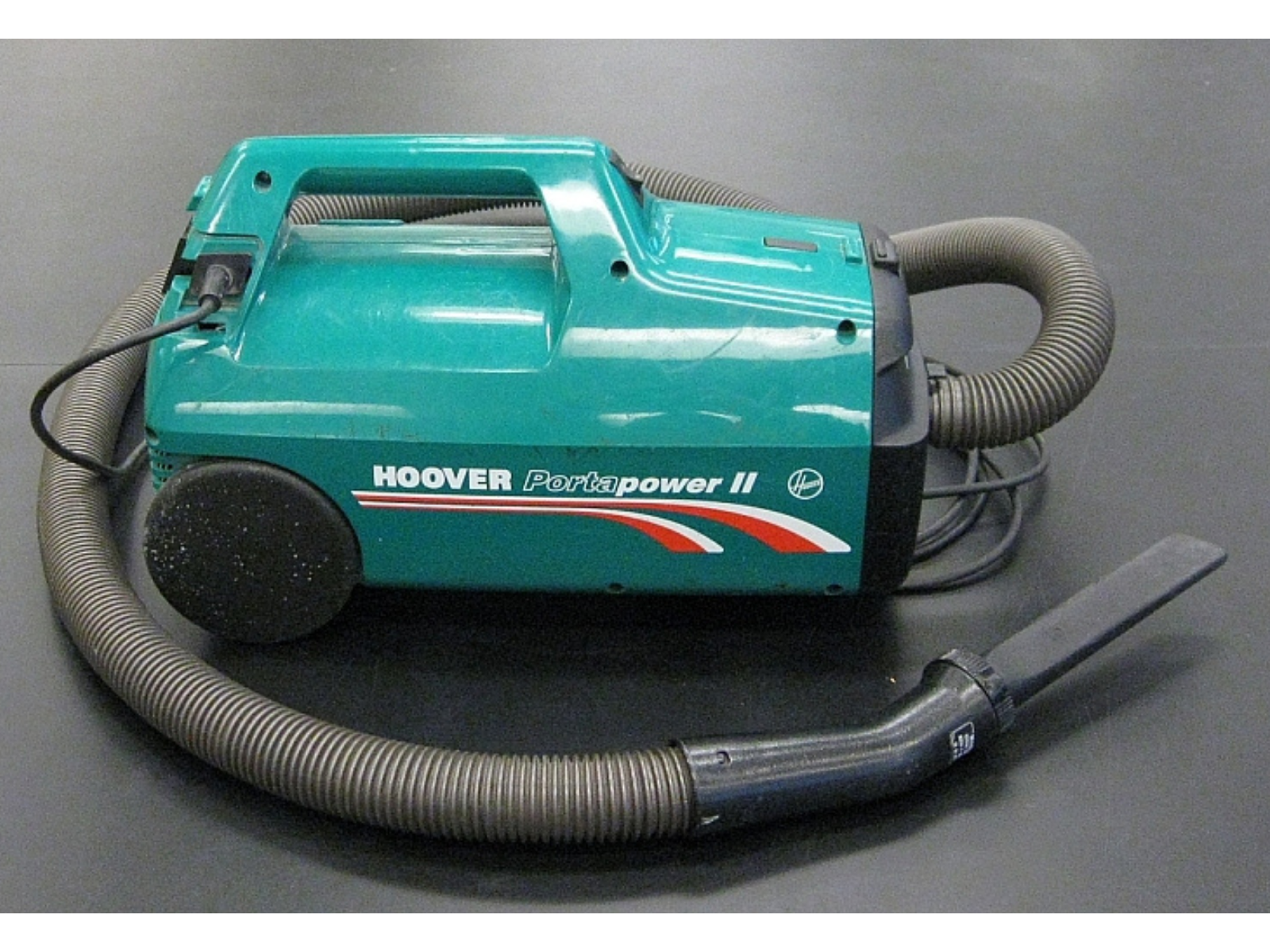 A teal bodied vacuum with a hose loosely wound around the body.