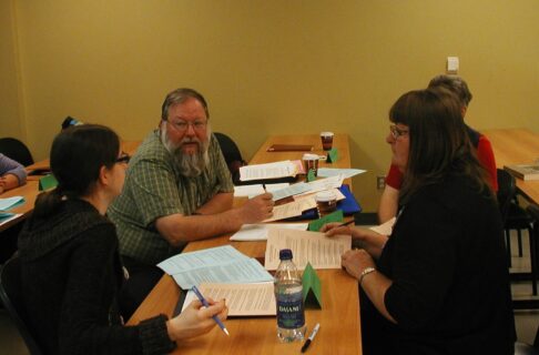 Four individuals sitting around a table in discussion with each other over papers and notebooks.