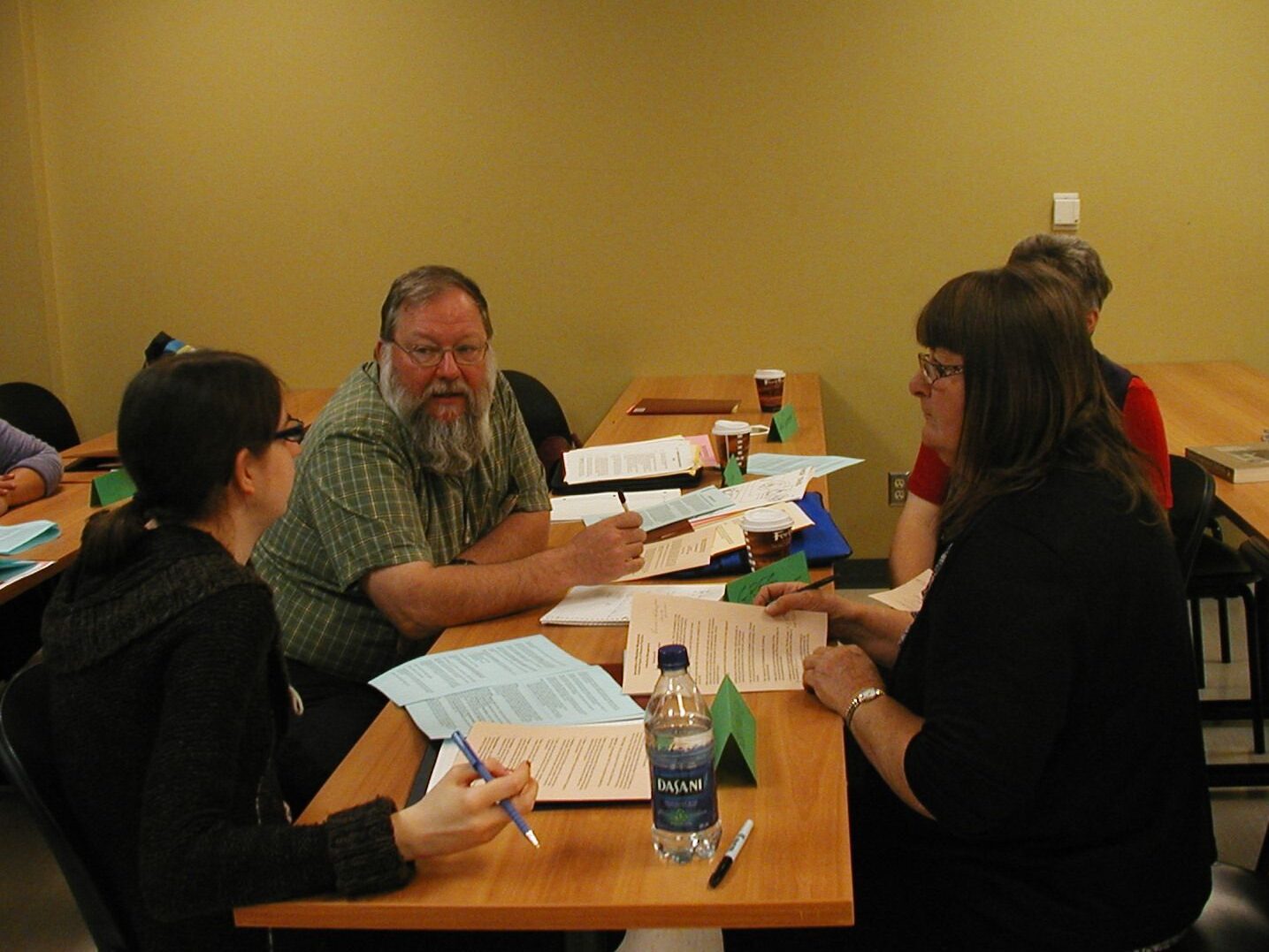 Four individuals sitting around a table in discussion with each other over papers and notebooks.