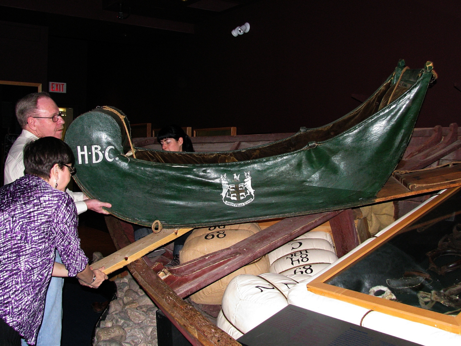Several individuals working together to lift down a green cariole sledge from display.