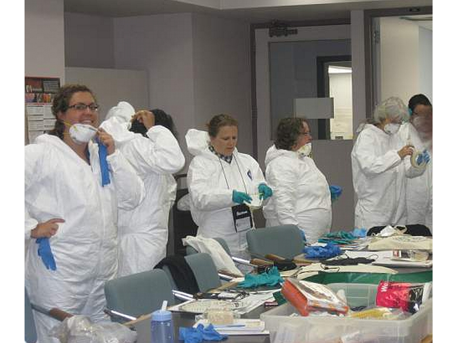 A row of people suiting up in white protective clothing and face masks.