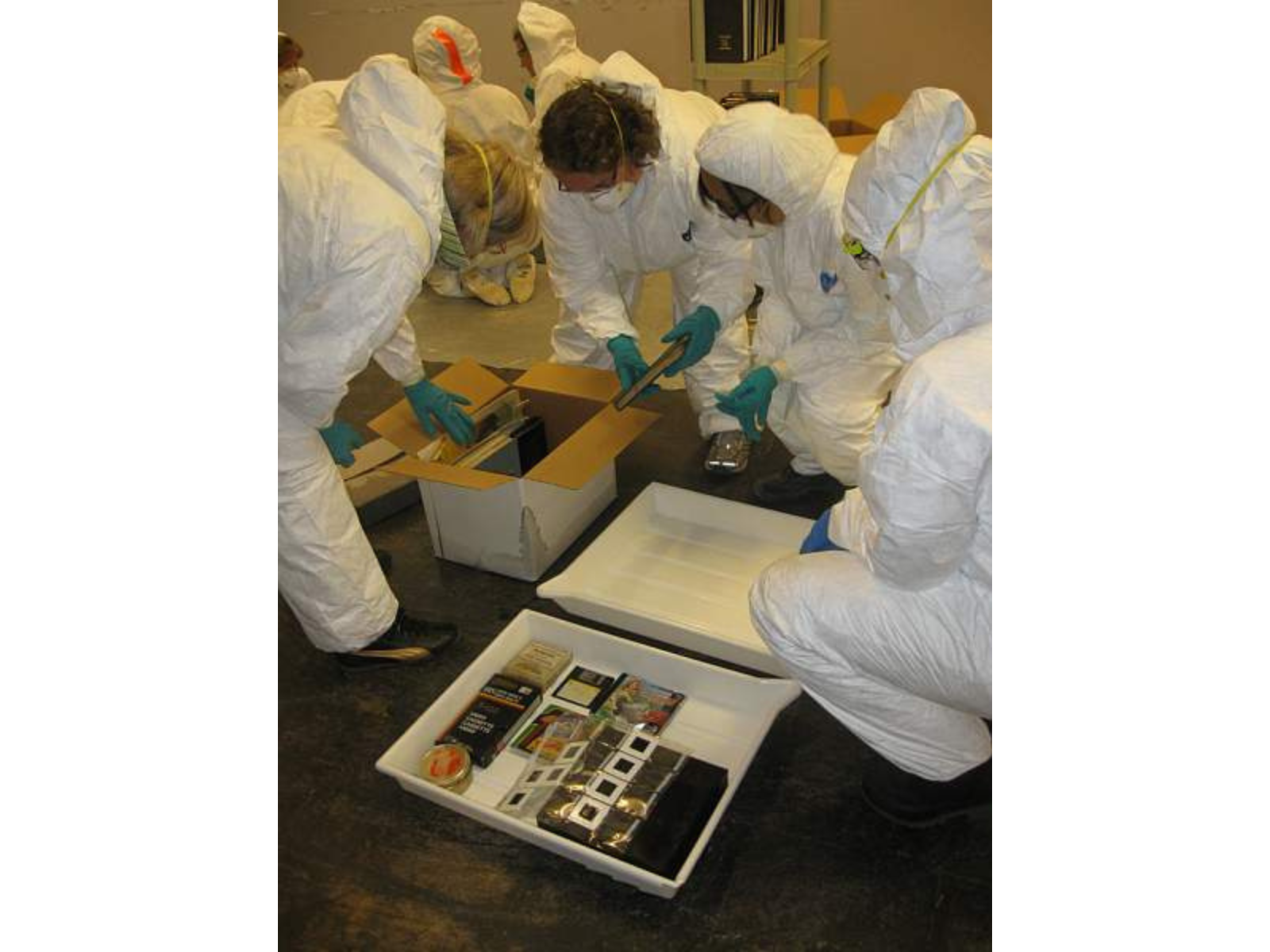 Four people wearing white protective clothing sorting various artifacts into trays and boxes.