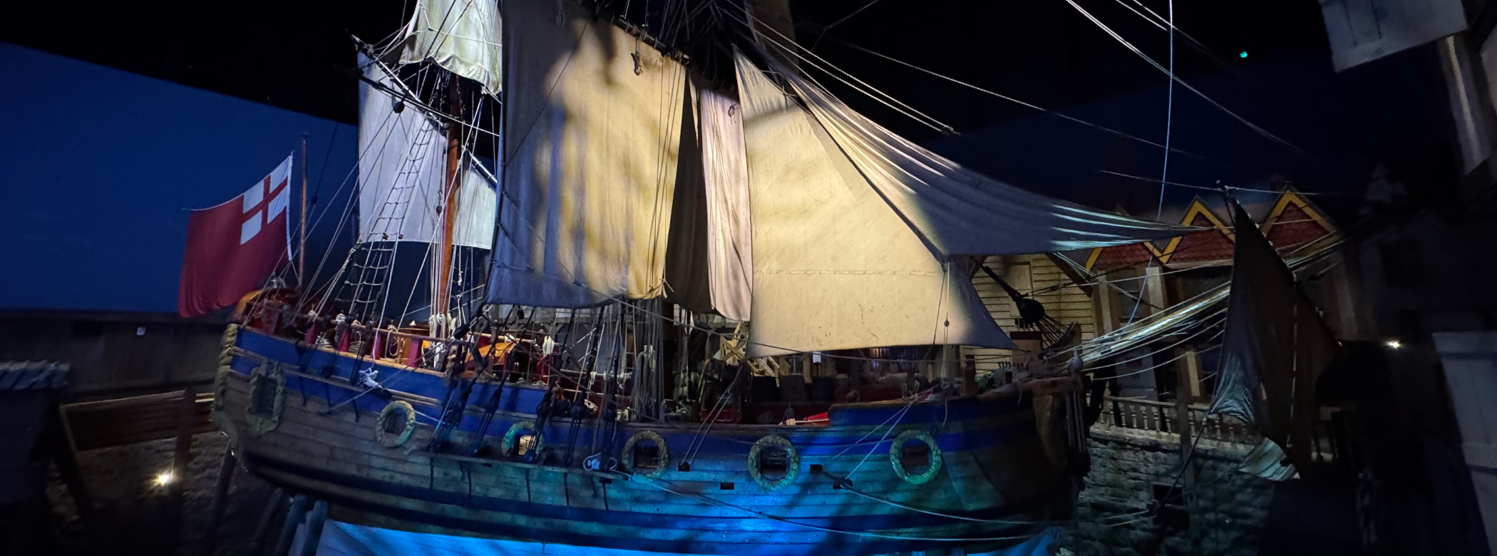 Photograph of a large wooden ship (the Nonsuch) with her sails out “in dock” in the Nonsuch Gallery of the Manitoba Museum.