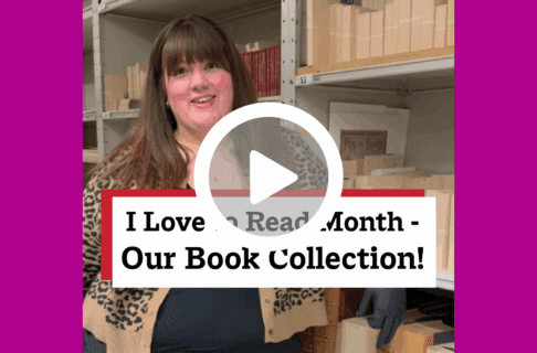 A screenshot of a video, an individual stands next to storage shelf lined with encased books. There's a play button over the screenshot and overlaid text reads, "I Love to Read Month / Our Book Collection!".