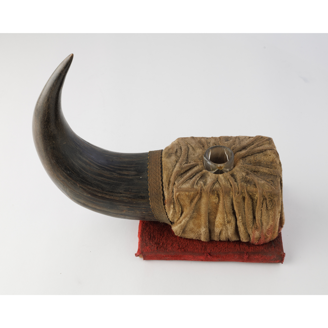 An inkwell set in a rough squared base, with a bison horn extending off the left side.