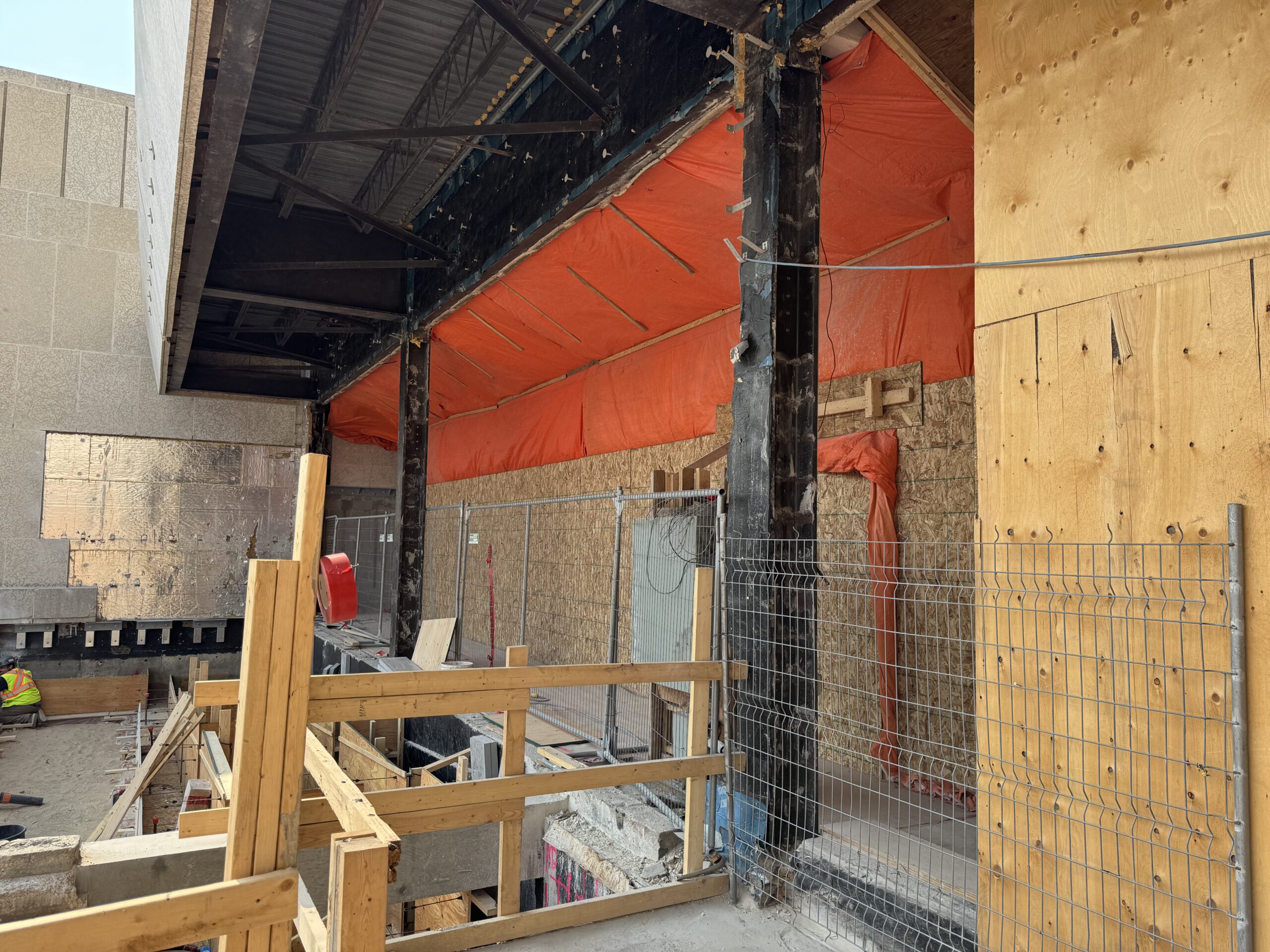 View from outside the museum looking towards teh Rupert Ave entrance. The main exterior wall has been removed and is instead walled by plywood and tarpaulins. On the ground a level down, board and rebar are in place to form the base of the new entrance ramp.
