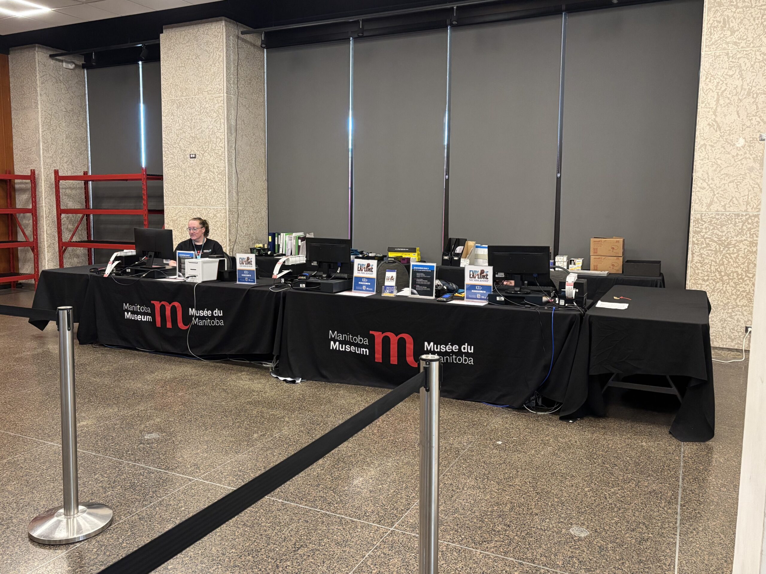 A Museum staff member seated at a temporary Box Office desk with three stations.