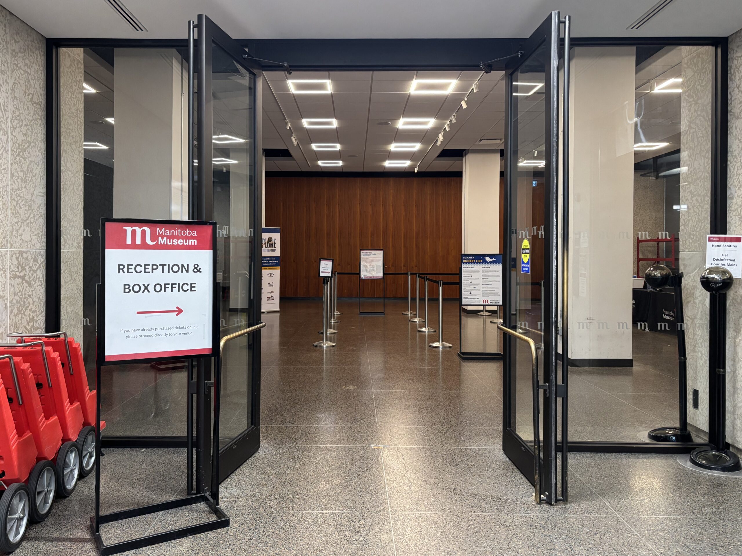 Looking through an open set of double doors into a room with stanchions creating a queue area. A sign beside the door reads, "Reception and Box Office".