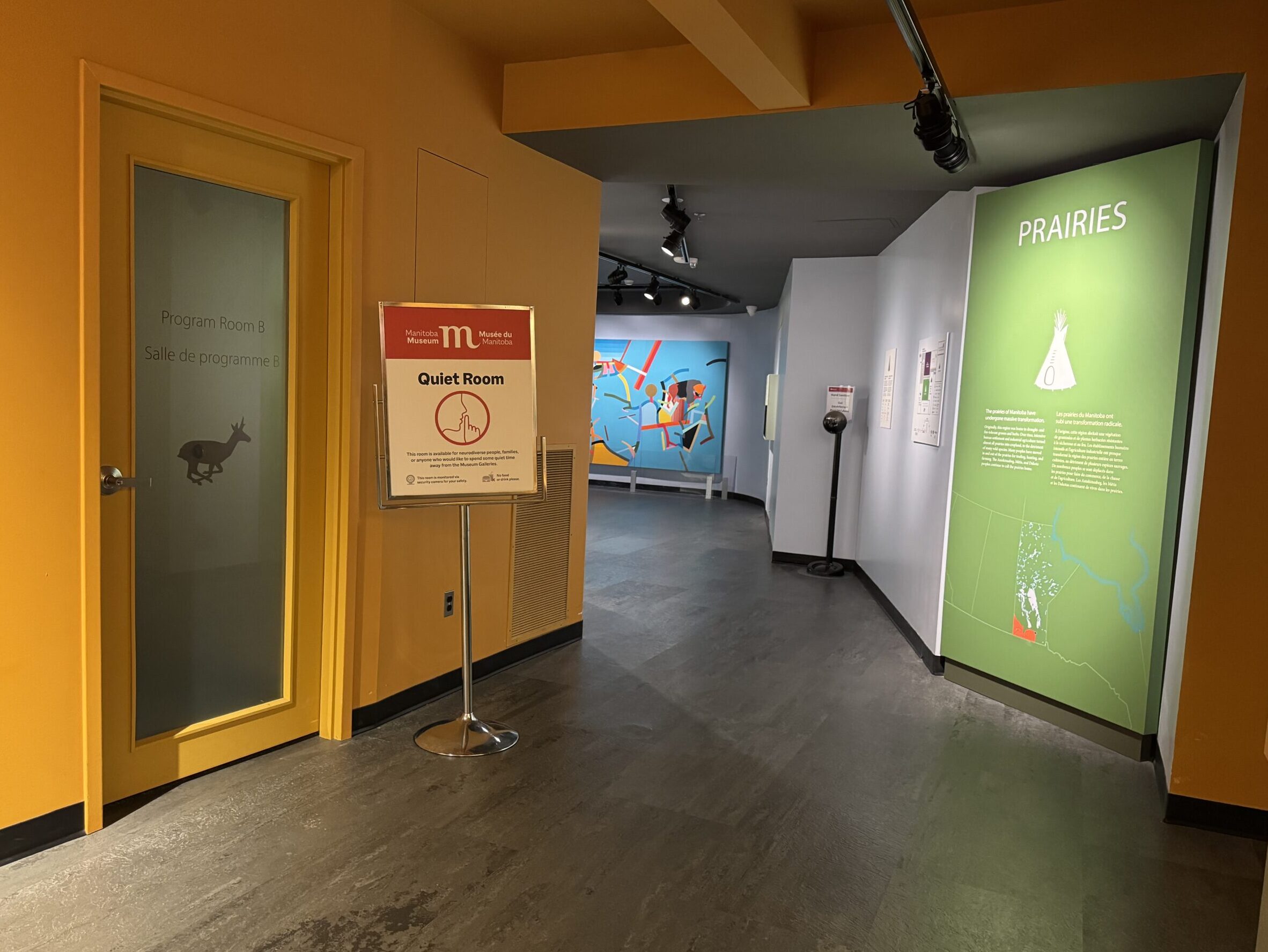 A hallway in the Museum Galleries with a frosted door leading to the Quiet Room on the left side, and the sign for the entrance to the Prairies Gallery on the right side.