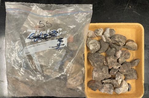A large freezer bag filled with dirt and excavated artifacts next to a plastic tub containing more of the same.