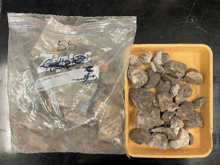 A large freezer bag filled with dirt and excavated artifacts next to a plastic tub containing more of the same.