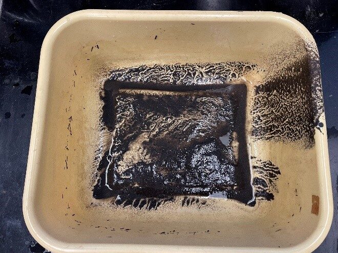 A cream coloured plastic basin with a dark, wet sludge at the base and along the side where the previous contents were poured out.