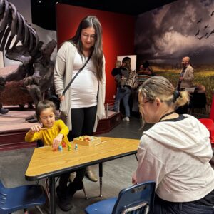 A young child sits at a low table playing with a magnetic fishing game as their parent and a Child Development Lab researcher observe and engage with them.