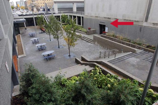 An arrow pointing to a door within a garden area with stairs, railings, trees and ramps.