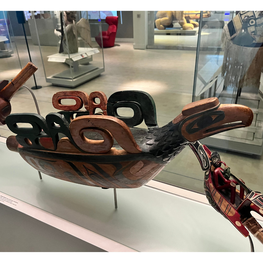 An ornately carved large wooden rattle in the shape of a thunderbird on display in a museum exhibit.