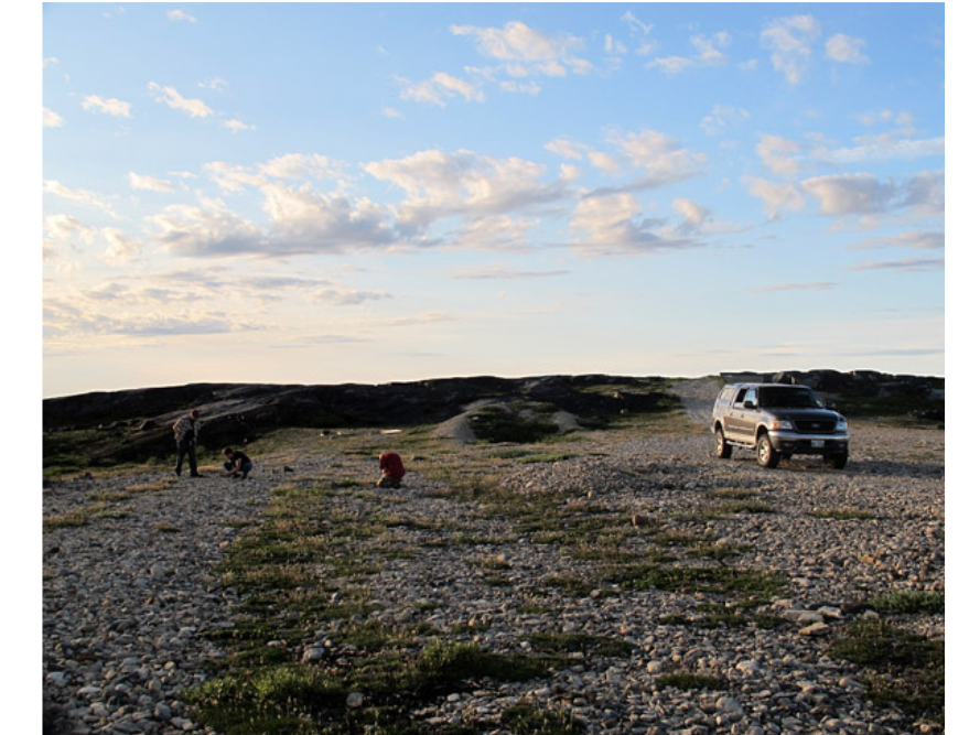 Wide-view shot of several people standing around taking photos and exploring on rocky ground near a parked pickup truck.