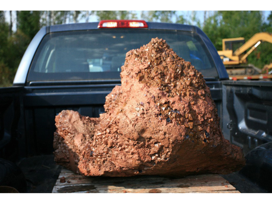 A large reddish boulder in the back of a pick-up truck.