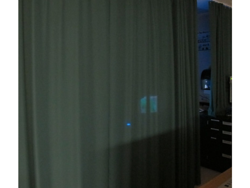 A computer screen shining through a curtain in a dark room.