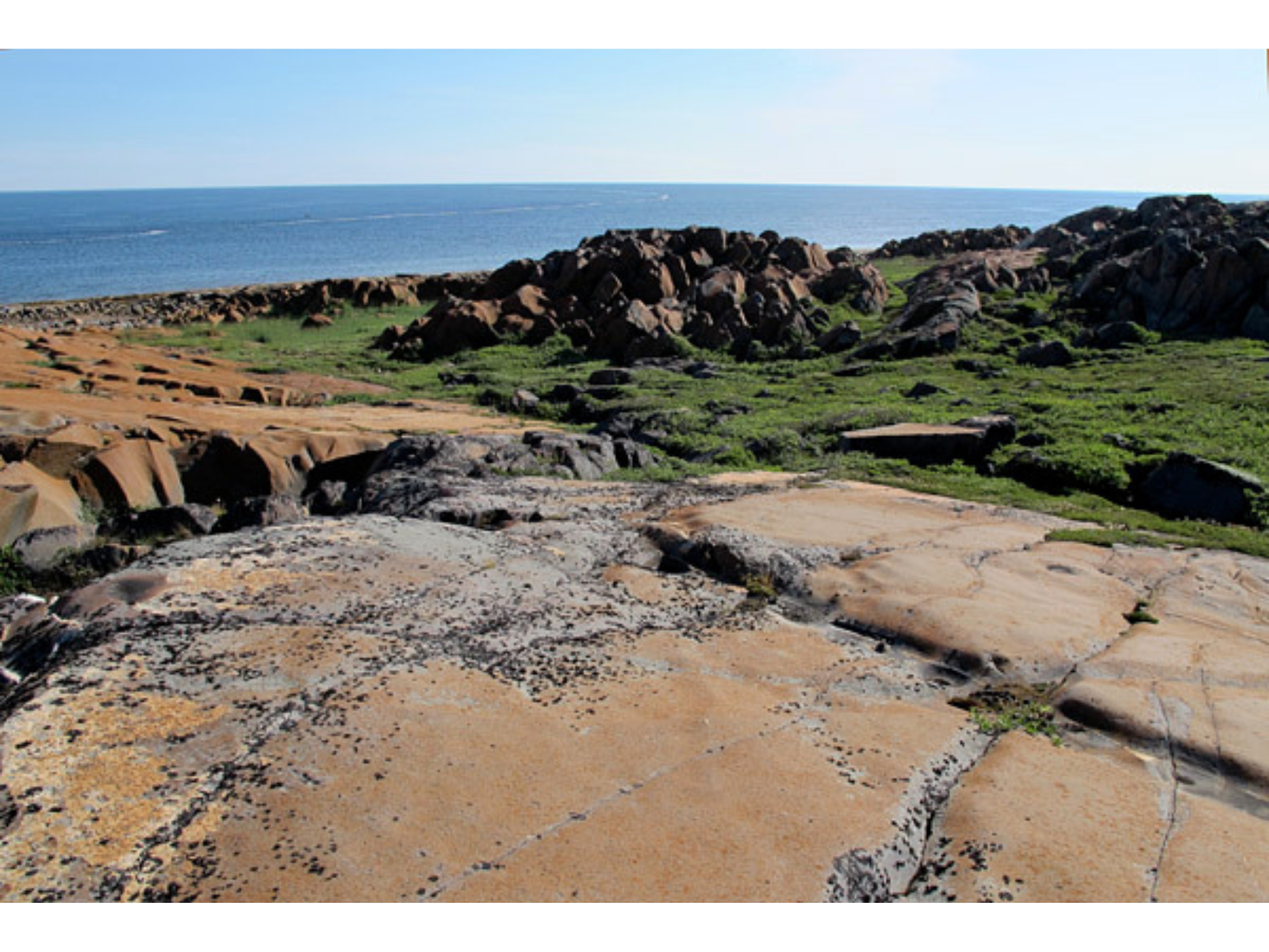 View out over a reddish rocky landscape leading towards a body of water.