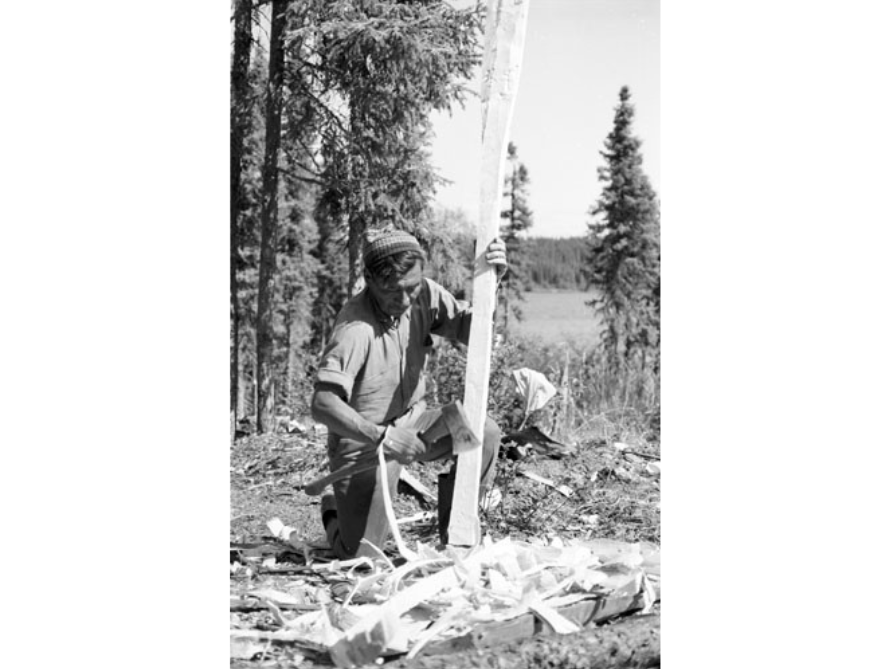 A black and white photo of a person using a tone tool to carve a wooden paddle.