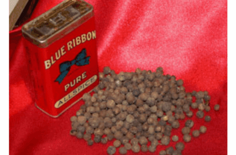 A small pile of allspice next to an allspice container on a red background.