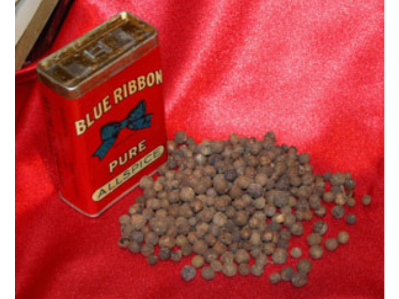 A small pile of allspice next to an allspice container on a red background.