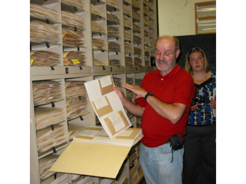 A museum staff person holding up a sheet of specimens from a museum storage drawer.