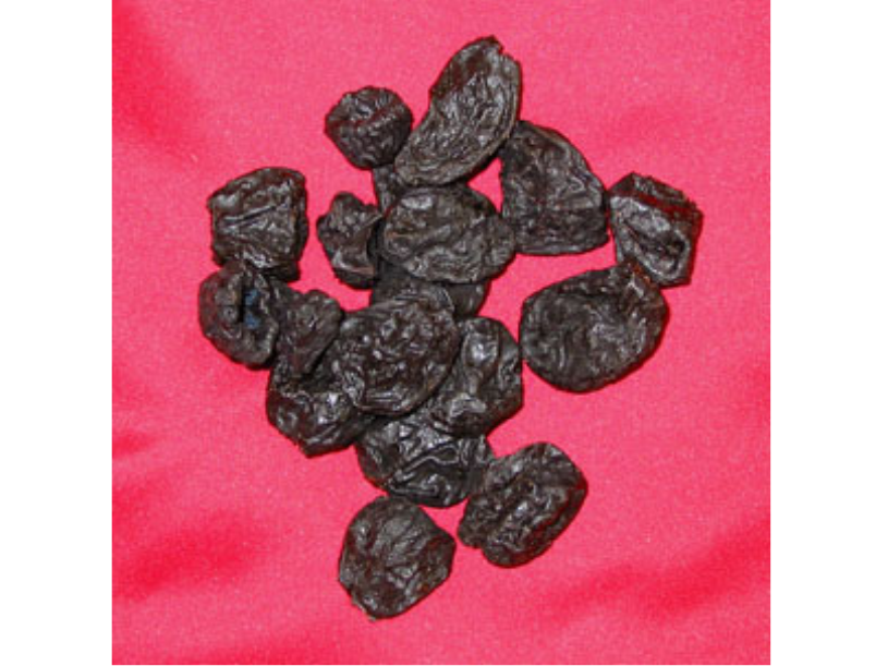 Small pile of dried prunes on a red background.