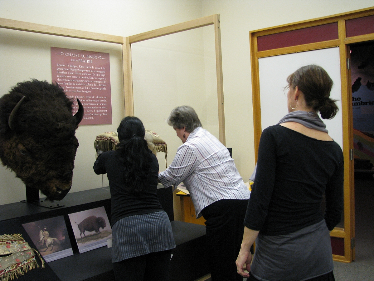 Three people around a display case, two of whom are adjusting a piece on a mount as the other looks on.