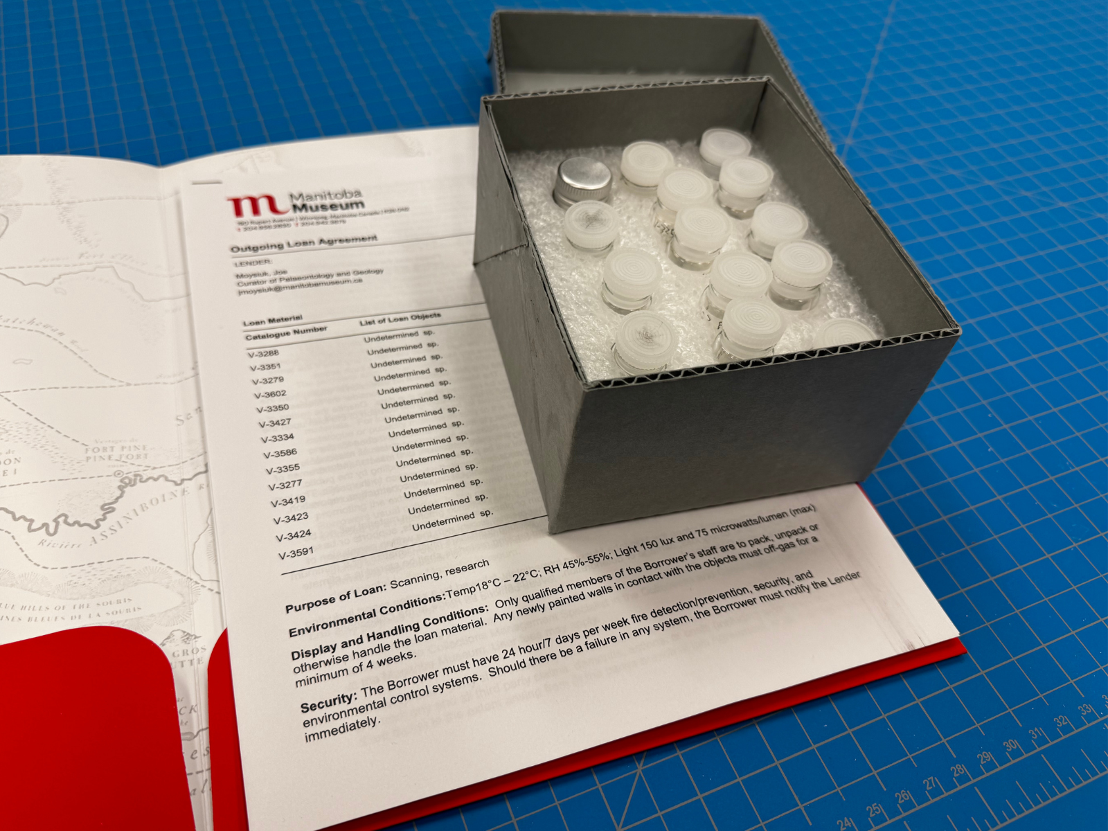 A small box containing a number of vials secured in foam. The box is atop an open file folder with an outgoing loan agreement document inside.