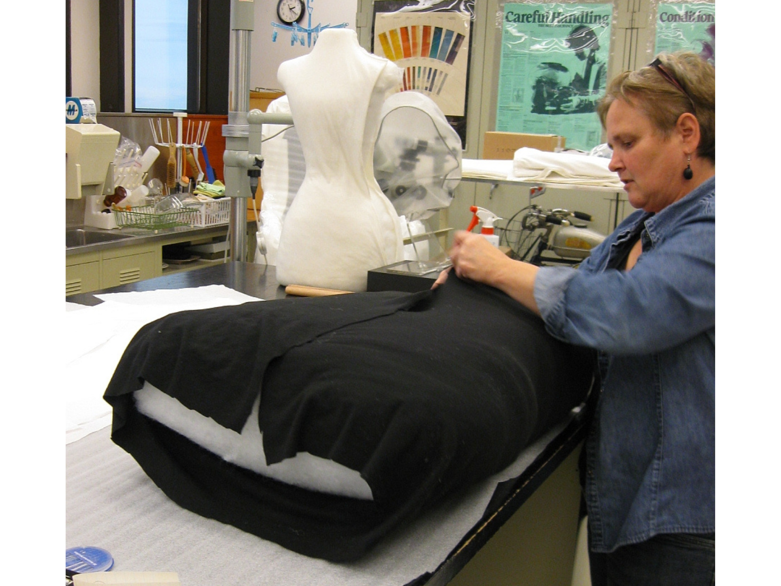 A layer of dark fabric being wrapped around a large carved block of foam on a table top.