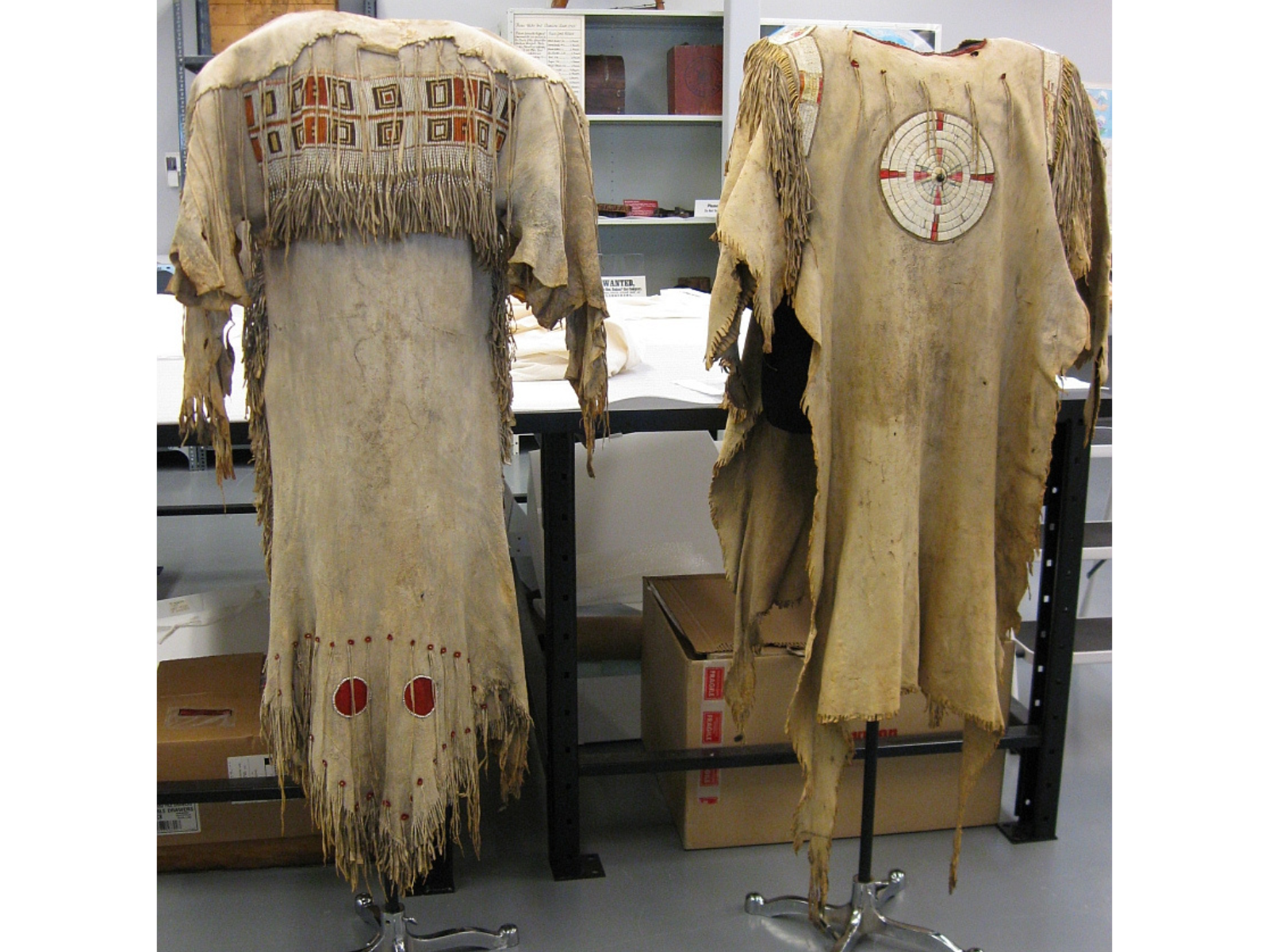A beaded and fringed hide dress and shirt each placed on standing mannequin stands.