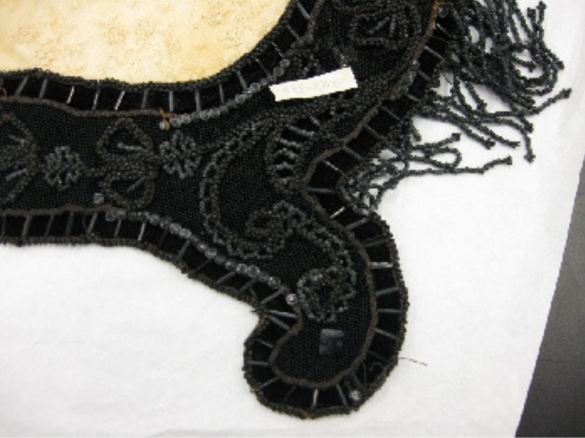 A collar of black velvet with light coloured beads. Some of the beads are a cloudy, whitish colour.
