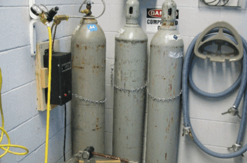 Three grey tanks of carbon dioxide standing against a wall.