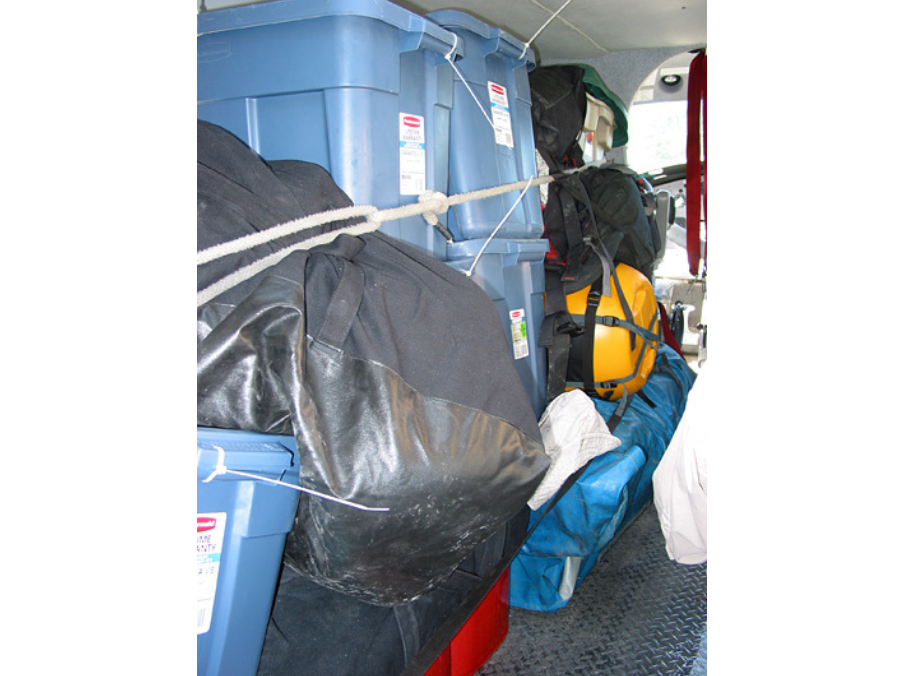 Tightly packed and bound gear in the back of a floatplane. Bins and bags are tied to the left side with some ropes.
