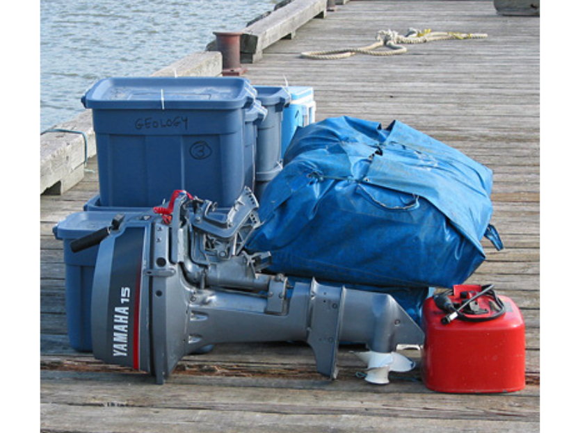 Pile of gear and a boat motor stacked on the dock of a lake.