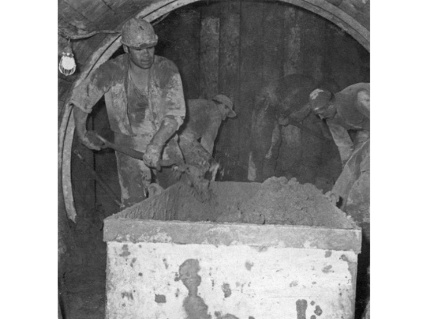 A black and white photograph of workers excavating a sewer in 1969 with shovels and a rail cart.