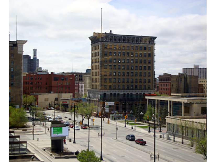 View looking south on Main Street towards the Winnipeg City Hall. The road is quiet under the midday sky.