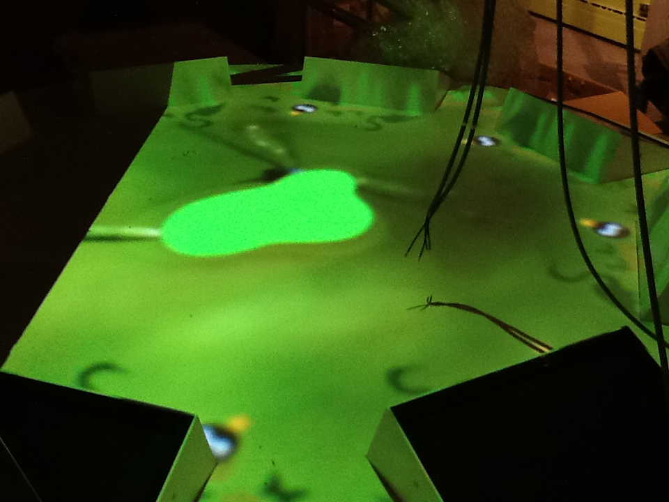 A round table with eight digital touchscreens embedded around the surface. A green light illuminates the tabletop with a "blob" near the centre brighter than the rest.