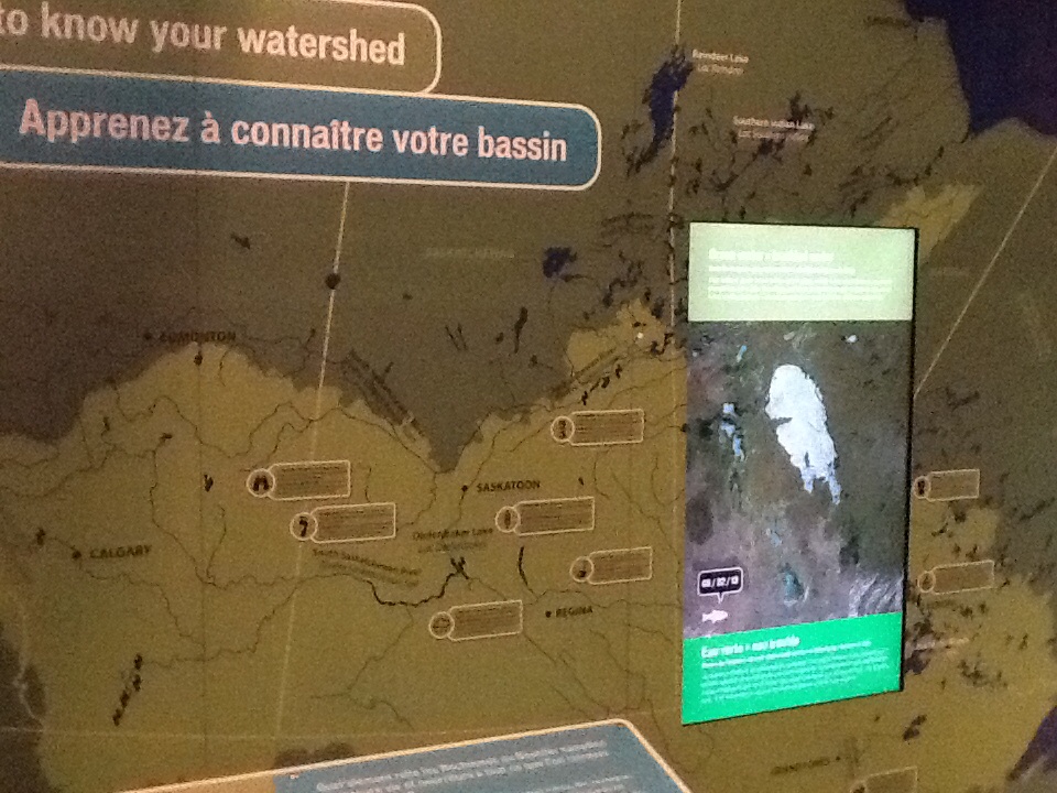 Close up on a Manitoba watershed map and digital touchscreen on an exhibit wall.