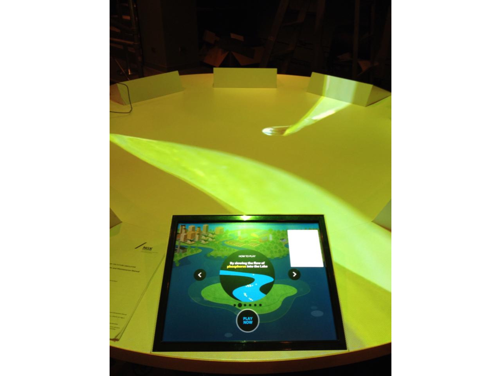 Looking at a touchscreen embedded in a round table lit with green. The screen shows a "How to Play" graphic.